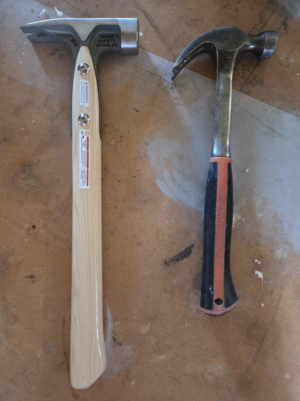 Dalluge 16 oz titanium hammer with a hickory handle and safety labels lying next to an older steel claw hammer on a plywood bench