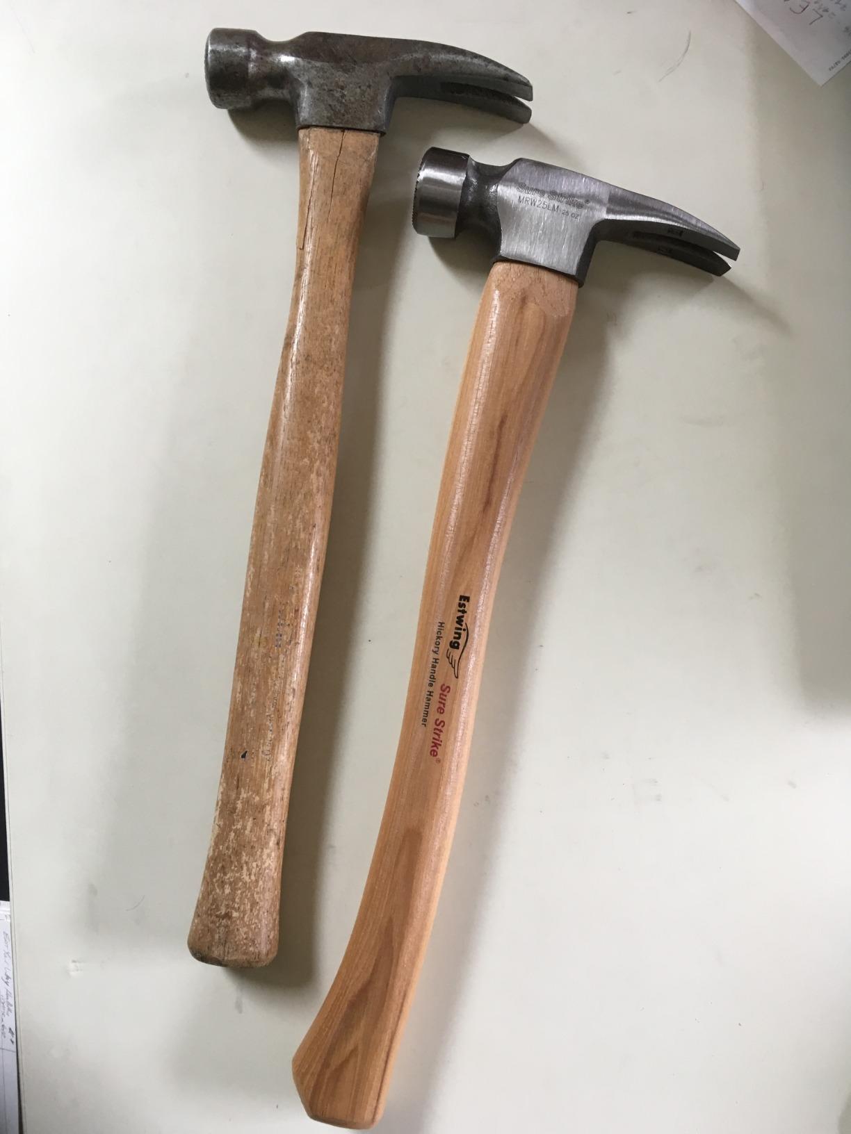 An old, worn wood-handled framing hammer next to a new framing hammer with a curved hickory handle on a white surface
