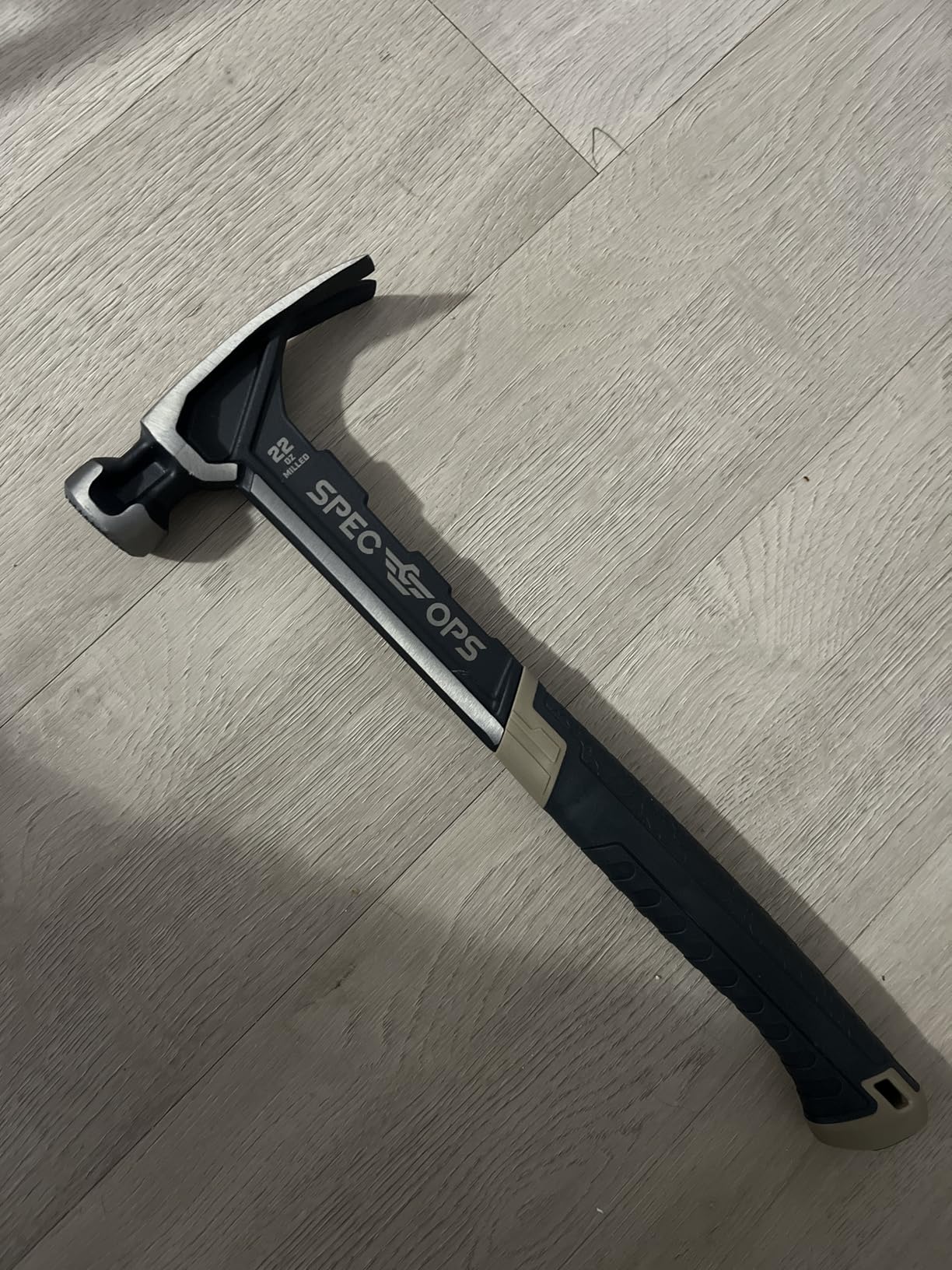 Black 22 oz framing hammer with a rubber grip lying on a light wood floor