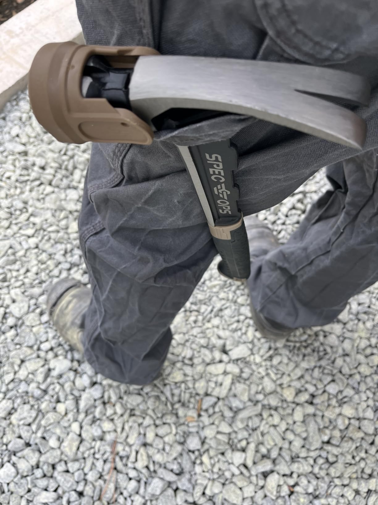 Framing hammer with a tan face cap hanging from the hammer loop of a pair of gray work pants